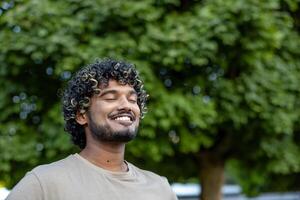Close-up of a man resting, relaxing and doing breathing exercises, smiling contentedly with his eyes closed, walking in a park among the trees. photo