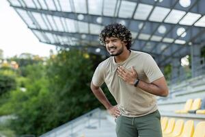 Overworked and overtired runner while doing active physical exercise and running outside in the fresh air, man holding hand on chest, severe heart pain, heart attack. photo