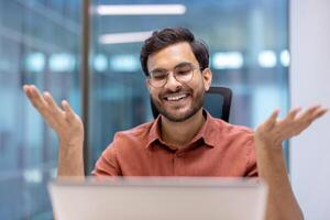 Business man smiling during call from office. He exudes positivity and communication. Ideal for concepts of remote work, virtual meetings, and professional interaction. photo