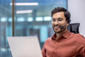 Businessman wearing headset focused on call. Office environment with large windows. Engaged in communication, showcasing professionalism and teamwork in corporate setting. photo