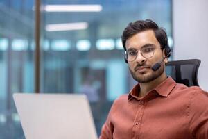 Latin American man businessman in headset focused working at laptop in modern office. Image portrays professional support, communication, technology in customer service environment. photo