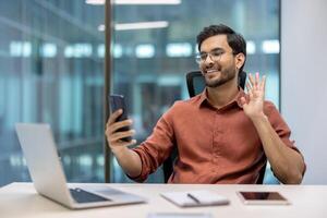 Confident young man in modern office using smartphone for call, engaging with colleague. Demonstrating happiness and connectivity through technology. Represents remote work, communication photo