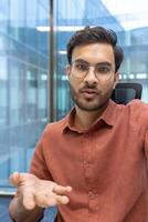 Businessman wearing glasses engaged in call gesturing with hand in modern office. Professional communication and interaction through phone. Confident expression, focused conversation photo