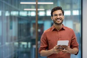 Smiling businessman holding tablet in office setting conveys confidence and engagement with technology. Professional environment highlights modern workplace dynamics and success. photo