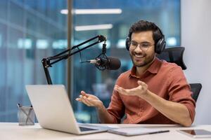 Podcast host engagingly speaks into microphone wearing headphones. In modern office setting, laptop open on desk. Host appears enthusiastic and professional, emphasizing dynamic photo