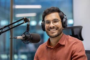Confident man with headphones smiling while speaking into microphone. Capturing essence of modern broadcasting and communication in recording studio. photo