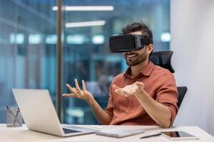 Business professional in modern office using virtual reality headset during call. Engaged in immersive experience seated with laptop. Concept technology, innovation, and digital communication photo