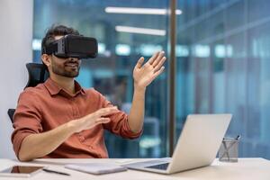 Man using VR headset immersed in virtual reality seated at office desk. Hands engaged in interaction with digital content. Modern workplace environment showcasing technology innovation and engagement photo