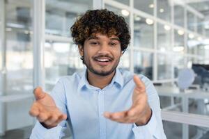 Smiling Indian businessman engaging in a call, expressing enthusiasm and friendliness in a modern office setting. photo