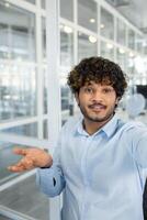 A smiling young man with curly hair makes a call from a modern office. He's looking at the camera, engaging in a friendly conversation. photo
