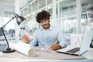 A focused male architect examining architectural models and blueprints in a modern office. He is analyzing designs and planning with concentration. photo