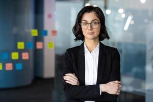 Young businesswoman in office setting with crossed arms, projecting confidence and professionalism. Surrounded by colorful sticky notes, symbolizing creativity and planning in modern workspace. photo