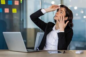 Businesswoman using eye drops at office desk, showing need for self-care during work hours. Focused on eye relief while working on laptop, capturing everyday office life. photo
