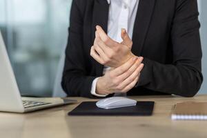 Businesswoman in office holding wrist in pain from computer use. Concept of workplace health, ergonomic issues, and computer strain. Emphasizes common office work challenges. photo