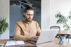 A focused office professional working on a laptop at a desk, emphasizing productivity, concentration, and modern workplace dynamics. photo