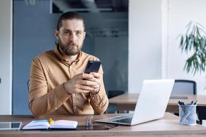 A professional individual sitting at a desk with a laptop, using a smartphone, creating a productive working environment. photo