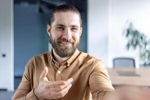 Webcam view, man inside office at workplace using smartphone app for call, talking to colleagues and partners while sitting at desk. photo