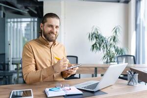 Confident professional taking notes while working on a laptop at a modern office desk, representing productivity and creativity in a workspace. photo