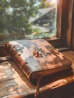 A leather book sits on a window sill with sunlight streaming in photo