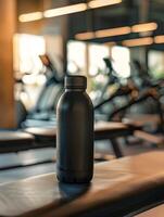 A black water bottle sitting on a bench in a gym photo