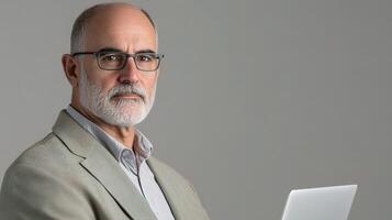 An older man with glasses and a beard is holding a laptop photo