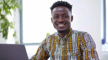 A man smiles while sitting at a desk with a laptop photo