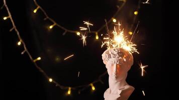 Sparklers in a Greek statue bust of David on a black background with Christmas lights. Sparklers explode in a vase in your head for New Year or Christmas Eve and deadline. Exclusive unique 2022 video