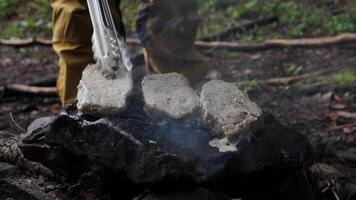 A hand man cooks meat, preparation steaks on a rock in the forest a close-up hike. Bonfire with fire for cooking in the field in nature video