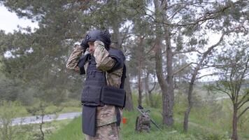 Young soldier in uniforms and tactical vest works in the forest and prepares for action at a temporary forest base. A man takes off his protective helmet after hard work in demining video