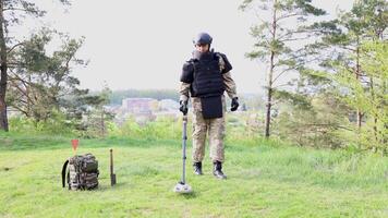 Man in a military uniform works in the forest with a metal detector video