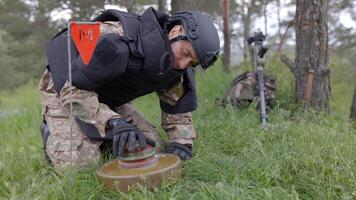 A man in a special suit works with a detector and found an explosive device. A man tries to neutralize an anti-tank mine. video