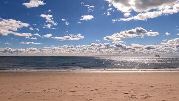 Timelapse of a sunny beach with sparkling ocean waves, Calm sandy beach with sparkling ocean waves under a bright sunny sky and fluffy clouds video