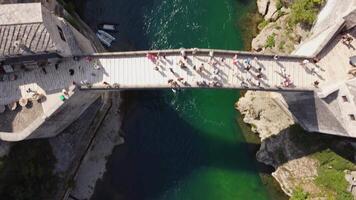 Top down view of the old bridge in Mostar. Aerial view of the Neretva River, boat and the famous bridge crossed by tourists video