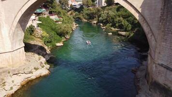 Mostar, Bosnia and Herzegovina, 08-26-2024, Tourist activity of boat ride in the Neretva river passing under the Stari Most, Mostar old bridge. Aerial view of the speedboat going in the river video
