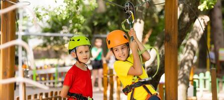 Small children climb a rope bridge in a rope park. Children are having fun in the adventure park. A female and male toddler on a climbing wall. Compliance with safety regulations. photo