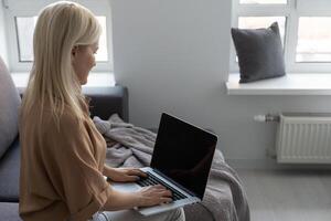 Smiling happy woman sitting on the sofa and using laptop. The concept of remote work or study during quarantine photo