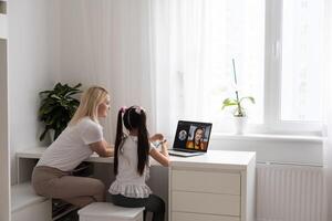 Private lesson. Attentive young woman tutor teacher help little girl pupil with studying math language correct mistakes explain learning material. Smiling mother assist small daughter with home task photo