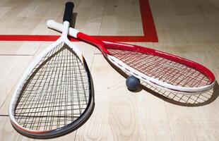 Two rackets and two squash balls lie on the parquet floor. Horizontal photo