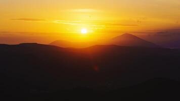 The sun sets against the backdrop of mountains and clouds of timelapse sunset video