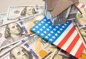 one hundred US dollar bill and a paper cut-out conditional image of a house against the background of the American flag photo