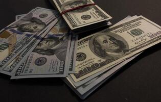 US Dollar bills bundles stack on black background. A pile of one hundred US banknotes with president portraits. Cash of hundred dollar bills, dollar background image with high resolution photo