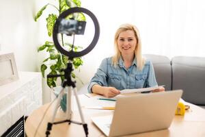 Calm clever woman standing in the bedroom in front of a camera on tripod and holding a roll of paper photo