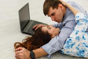 Couple Use Laptop Computer, while Sitting on the Living Floor room of their Apartment. Boyfriend and Girlfriend Talk, Shop on Internet, Choose Product to Order Online, Watch Streaming Service. photo