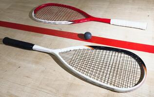 Two rackets and two squash balls lie on the parquet floor. Horizontal photo