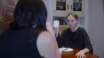 Mother and daughter talking while having drink at table. Females wearing casuals are sitting together at home. They are spending leisure time. video