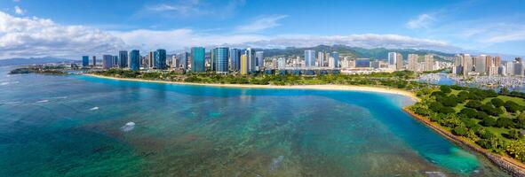 Aerial view of Honolulu, Oahu, showing Waikiki Beach, turquoise waters, lush parks, high rise buildings, and the Ko olau mountain range under a clear sky. photo