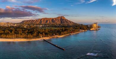 Aerial view of Waikiki Beach in Honolulu, Oahu, Hawaii, with Diamond Head Crater in the background, high rise buildings, and a vibrant sunset sky. photo