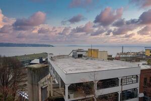 View of Seattle featuring a white building with large windows, Puget Sound in the background, distant landmasses, and colorful clouds at sunset. photo