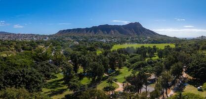 Aerial view of Diamond Head Crater on Oahu Island, Hawaii, with lush parkland, urban areas, and the ocean visible under a clear blue sky. photo