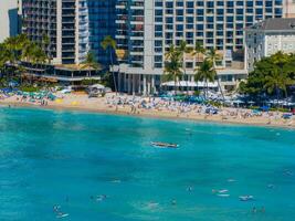 Turquoise waters, sandy beach, high rise hotels, palm trees, colorful umbrellas, and people enjoying paddleboarding and outrigger canoe rides. photo